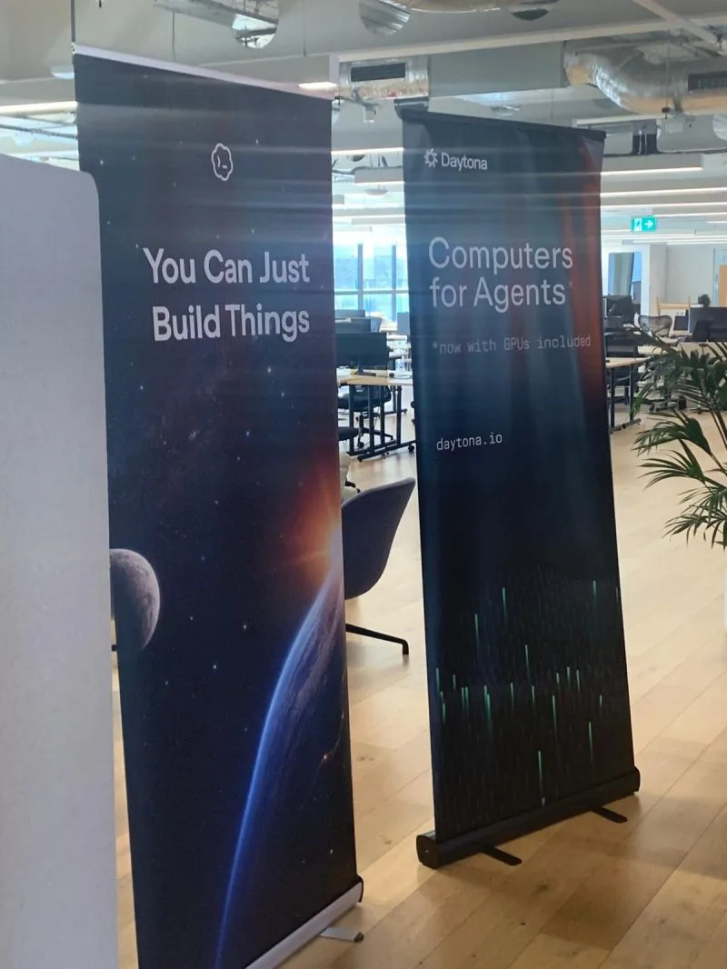 Two pull-up banners in an open office, one reading You Can Just Build Things and one reading Daytona, Computers for Agents