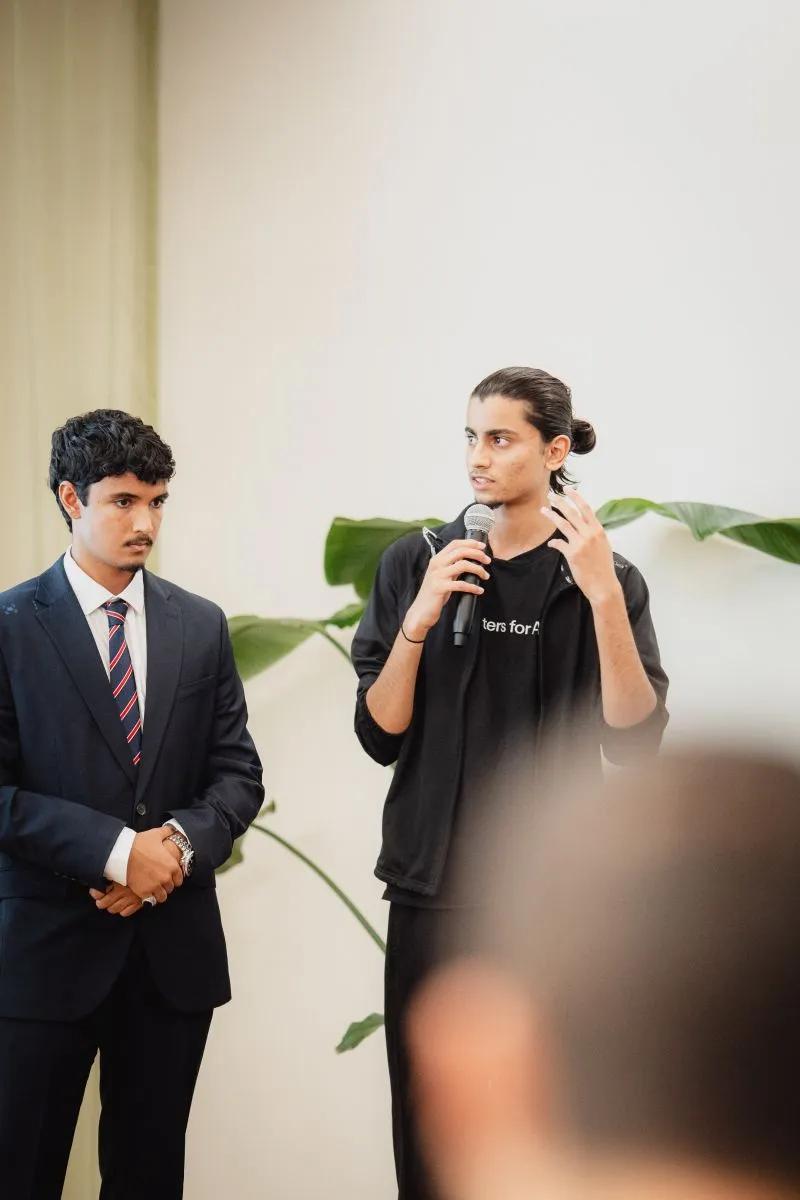 Rayhan answering a question with a microphone, a teammate in a suit standing beside him